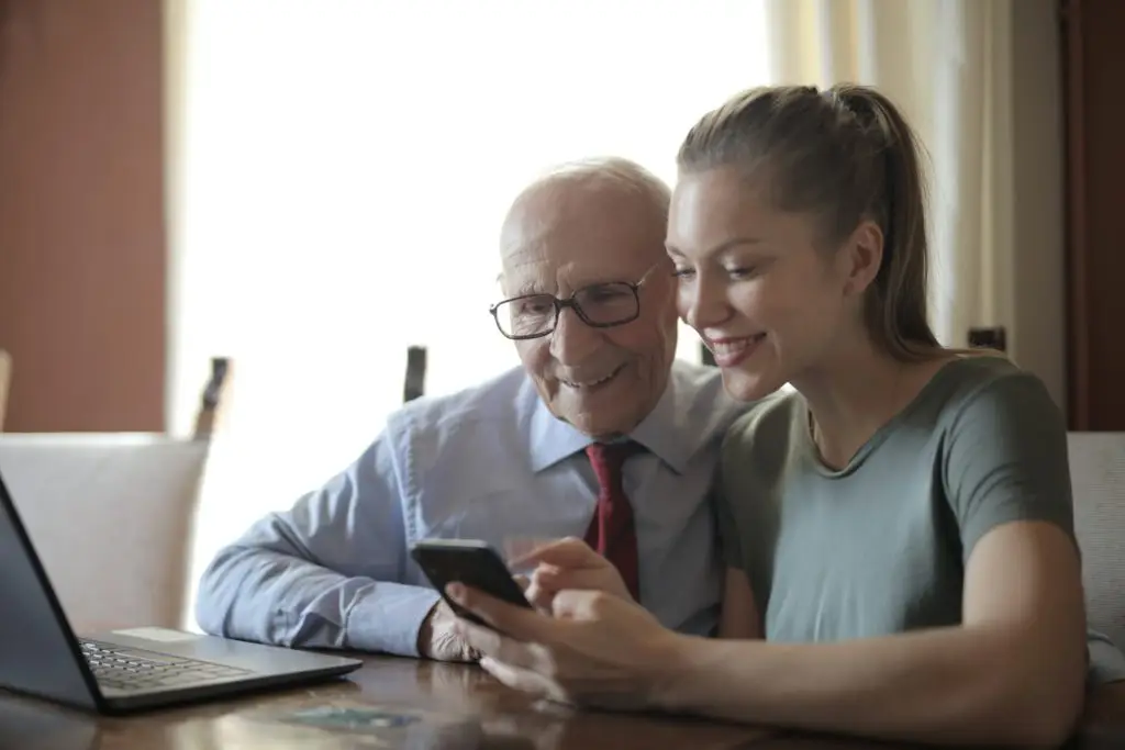 Young woman and elderly man looking at Elders' Helpers respite care services on a phone.