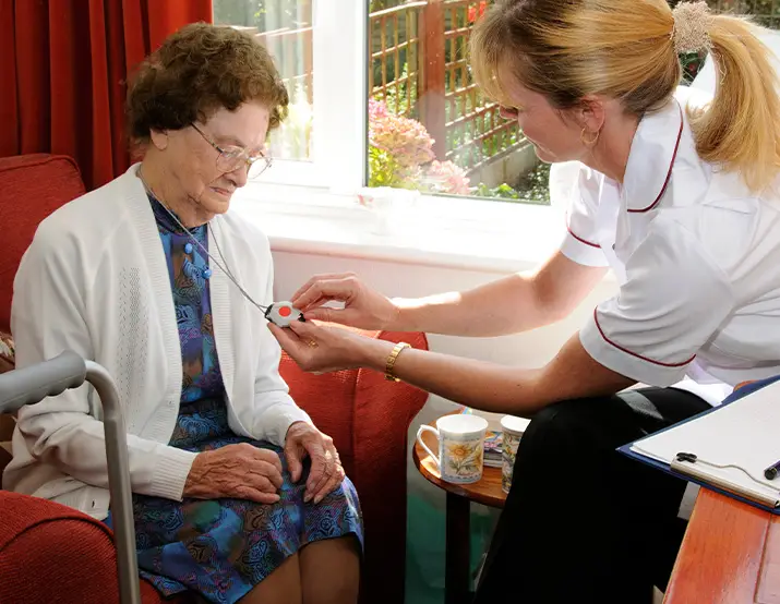 Nurse demonstrating how to use the Personal Emergency Response System (PERS) to an elderly lady.